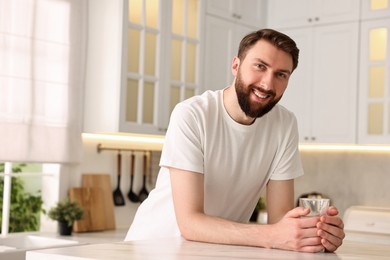 Happy young man with glass of water in kitchen at morning