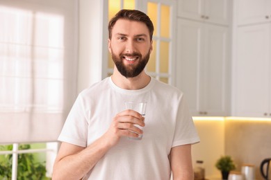 Happy young man with glass of water in kitchen at morning