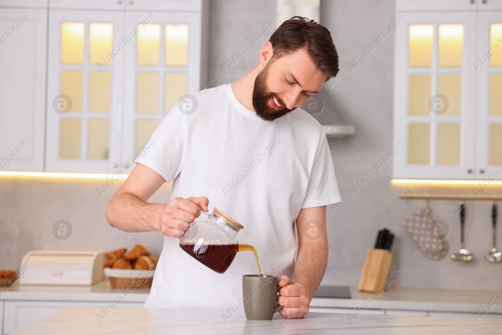 Photo of Happy young man pouring coffee into cup in kitchen at morning