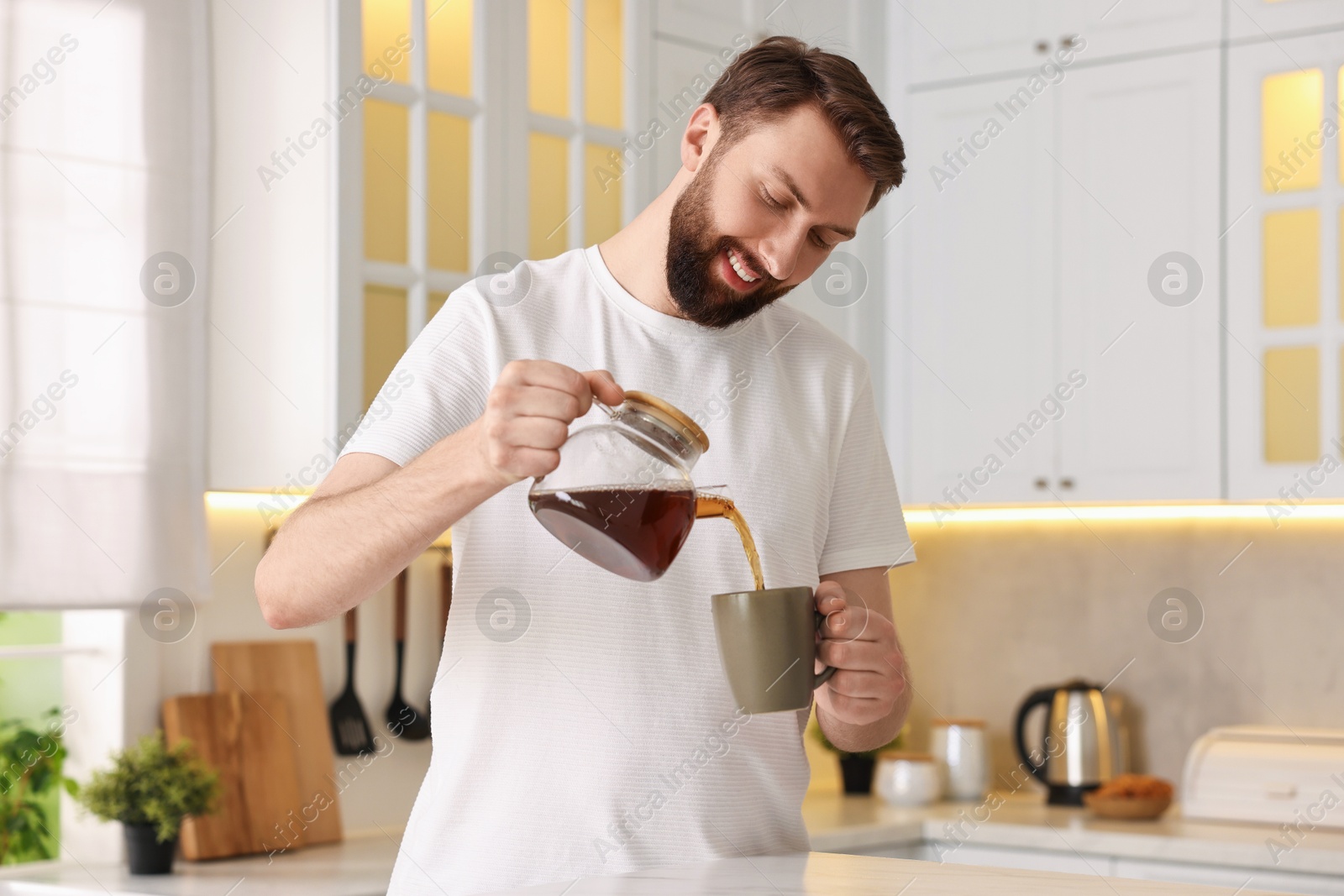 Photo of Happy young man pouring coffee into cup in kitchen at morning