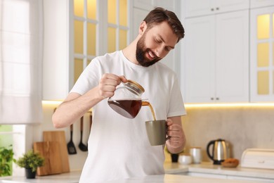 Happy young man pouring coffee into cup in kitchen at morning