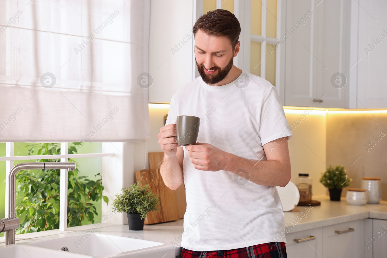 Photo of Happy young man with cup of coffee in kitchen at morning