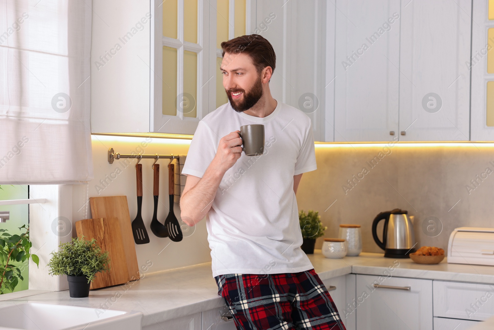 Photo of Happy young man with cup of coffee in kitchen at morning