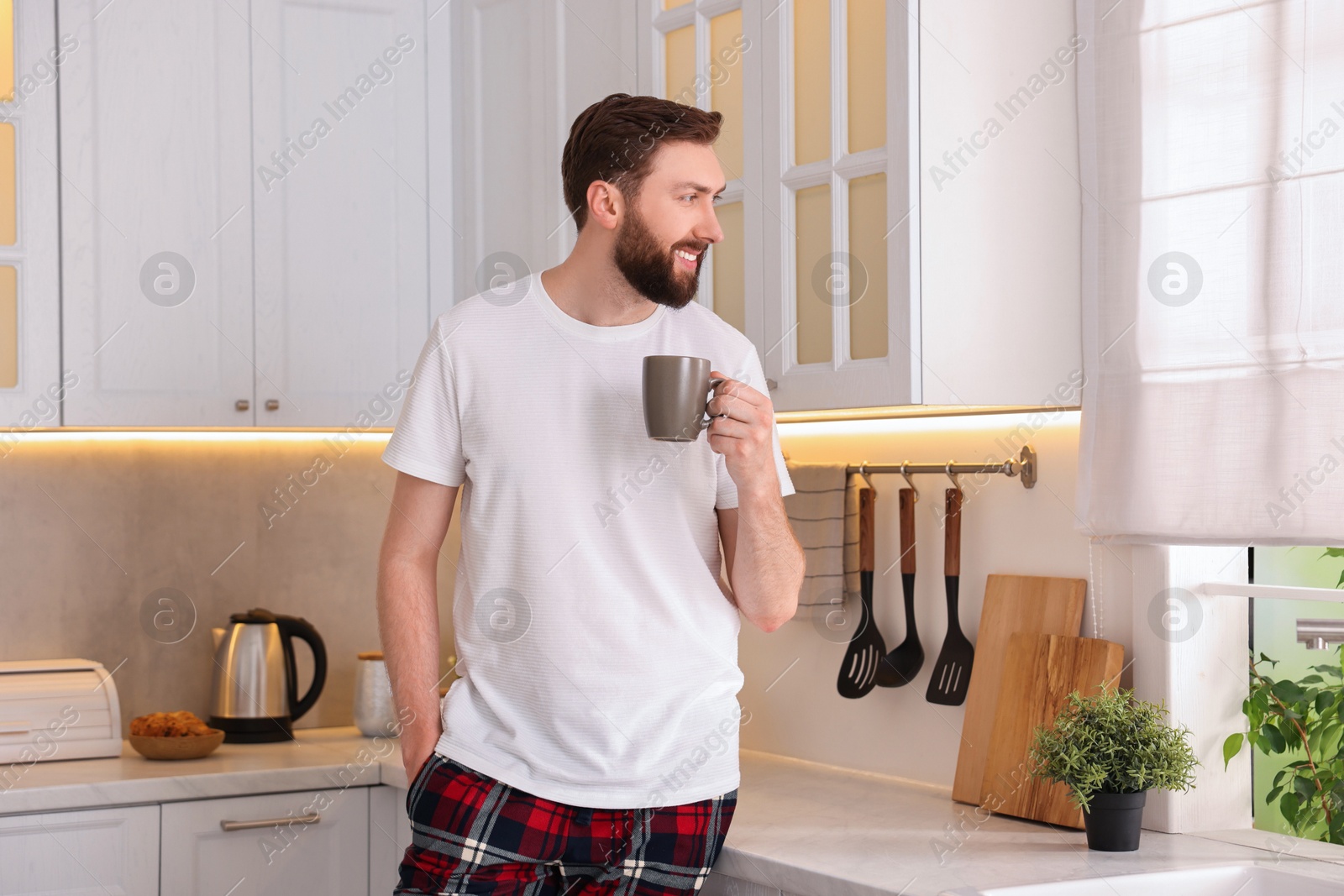 Photo of Happy young man with cup of coffee in kitchen at morning