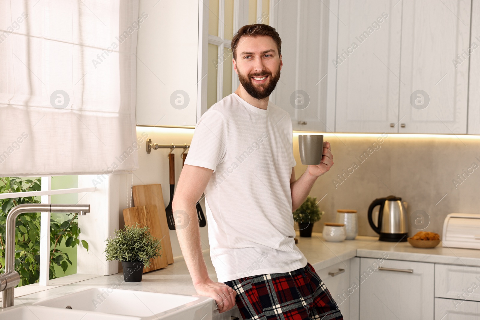 Photo of Happy young man with cup of coffee in kitchen at morning