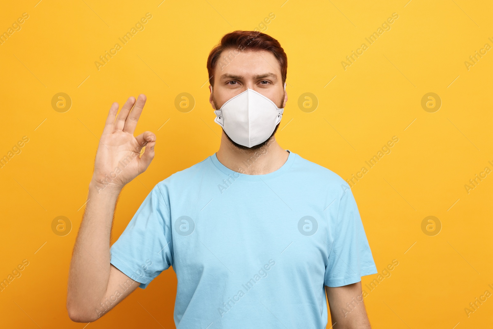Photo of Man in respirator mask showing OK gesture on yellow background