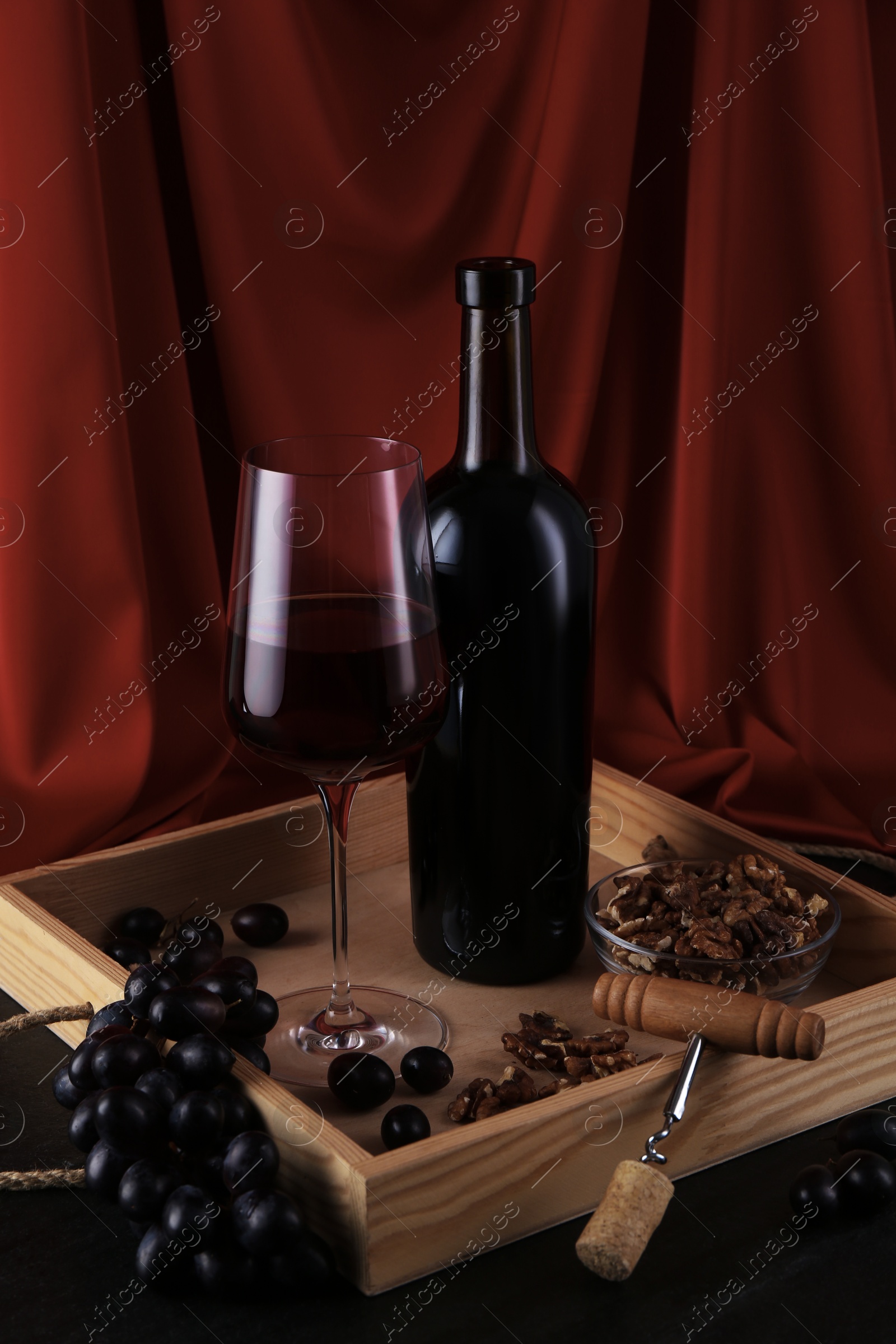 Photo of Corkscrew, glass of wine, bottle and grapes on black table