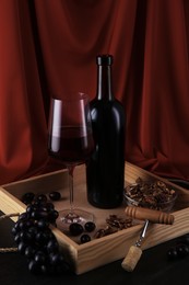 Photo of Corkscrew, glass of wine, bottle and grapes on black table