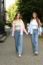 Photo of Twin sisters holding hands while walking outdoors