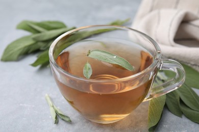 Aromatic herbal tea in cup with sage on grey table, closeup