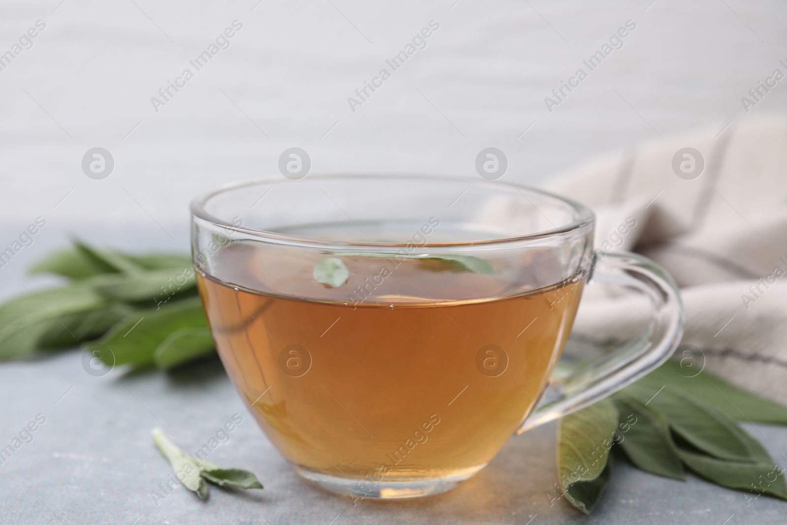 Photo of Aromatic herbal tea in cup with sage on grey table, closeup