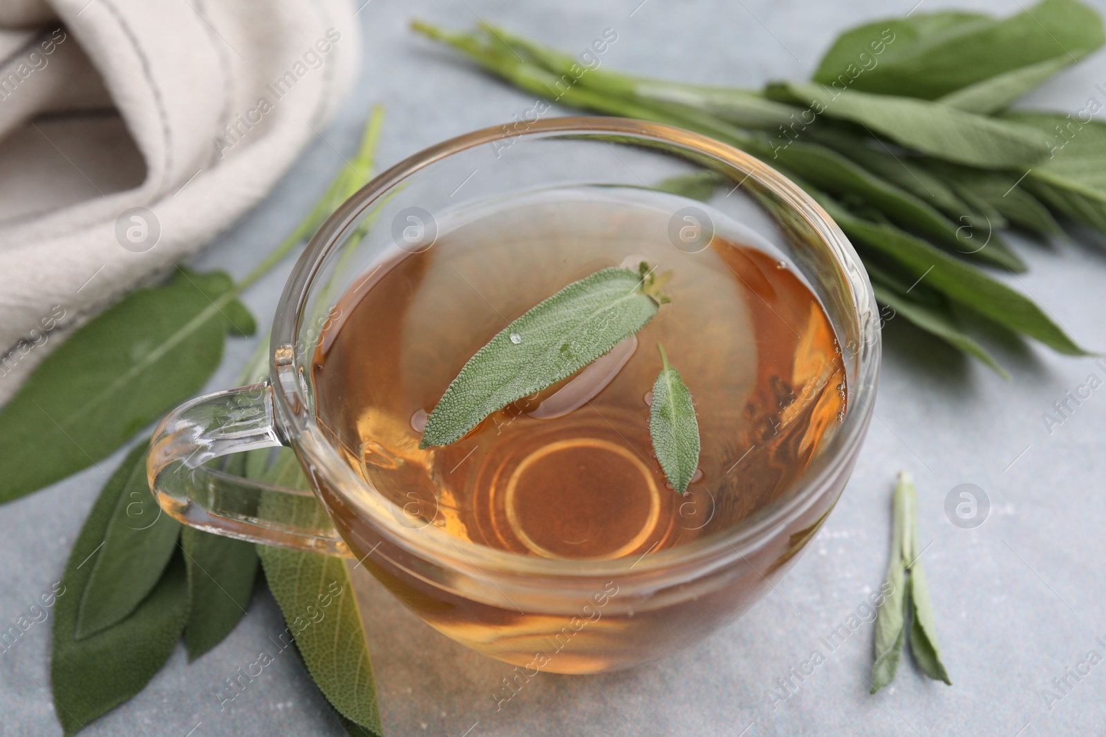 Photo of Aromatic herbal tea in cup with sage on grey table, closeup