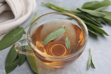 Aromatic herbal tea in cup with sage on grey table, closeup