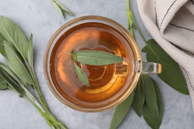 Aromatic herbal tea in cup with sage on grey table, top view