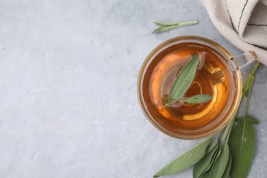 Aromatic herbal tea in cup with sage on grey table, top view. Space for text