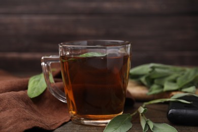 Aromatic herbal tea in cup with sage on wooden table, closeup