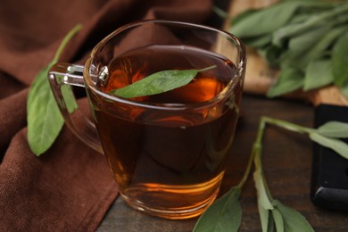 Aromatic herbal tea in cup with sage on wooden table, closeup