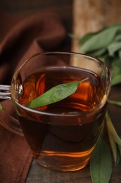 Aromatic herbal tea in cup with sage on wooden table, closeup