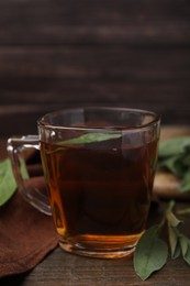 Aromatic herbal tea in cup with sage on wooden table, closeup