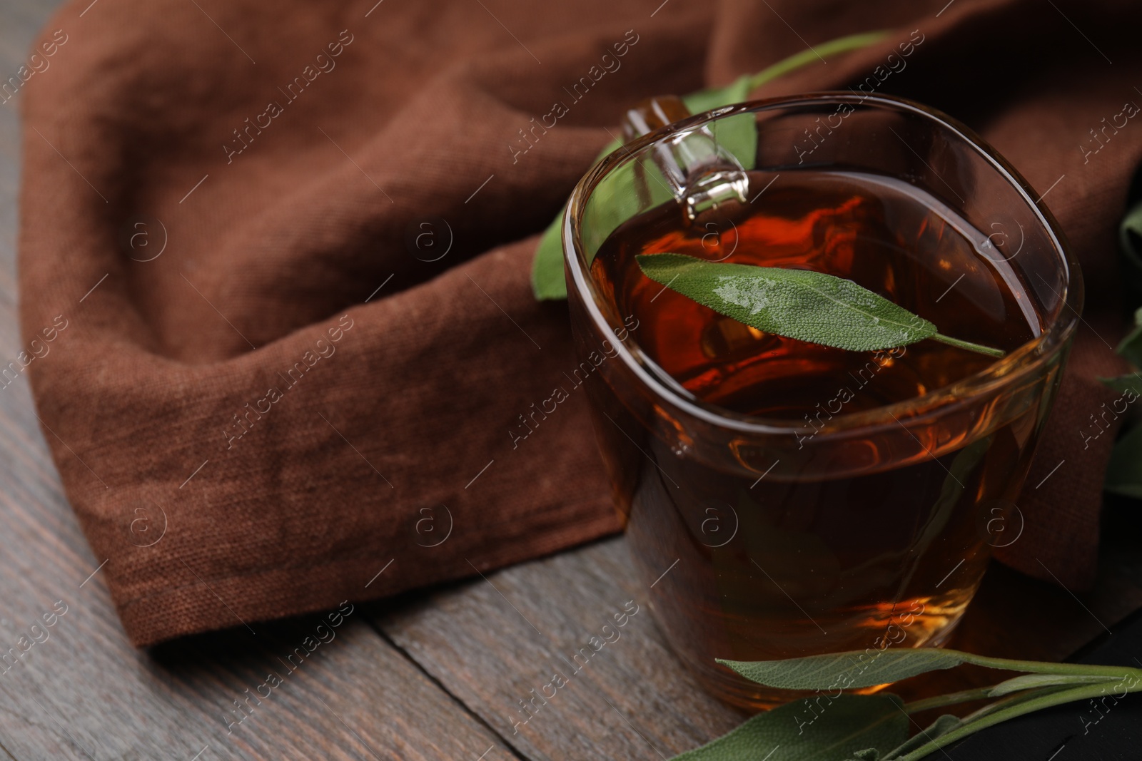 Photo of Aromatic herbal tea in cup with sage on wooden table, space for text