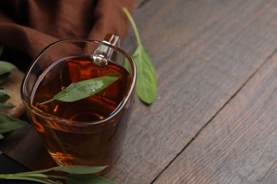 Photo of Aromatic herbal tea in cup with sage on wooden table, space for text