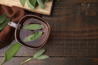 Aromatic herbal tea in cup with sage on wooden table, top view. Space for text