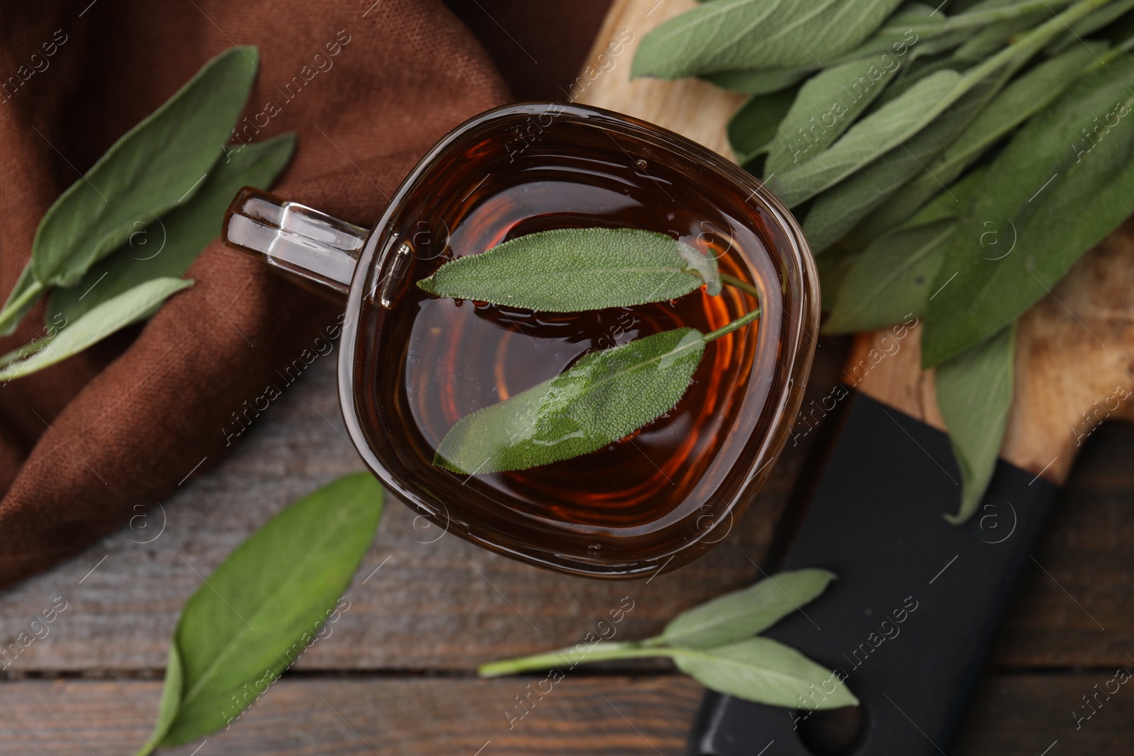 Photo of Aromatic herbal tea in cup with sage on wooden table, top view