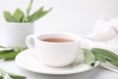 Aromatic herbal tea in cup with sage on white table