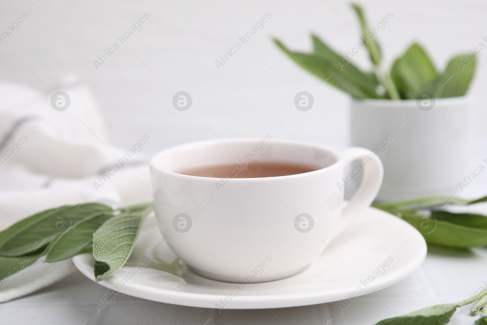 Photo of Aromatic herbal tea in cup with sage on white table