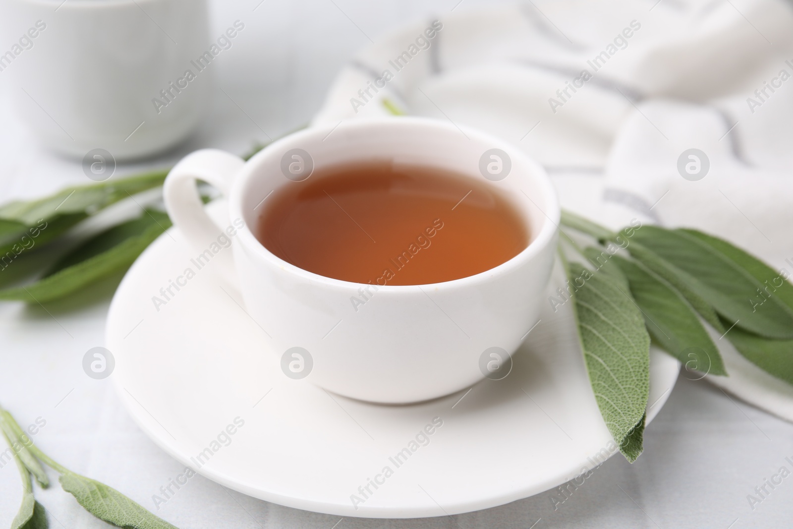 Photo of Aromatic herbal tea in cup with sage on white table