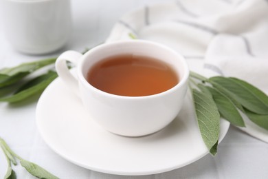 Aromatic herbal tea in cup with sage on white table