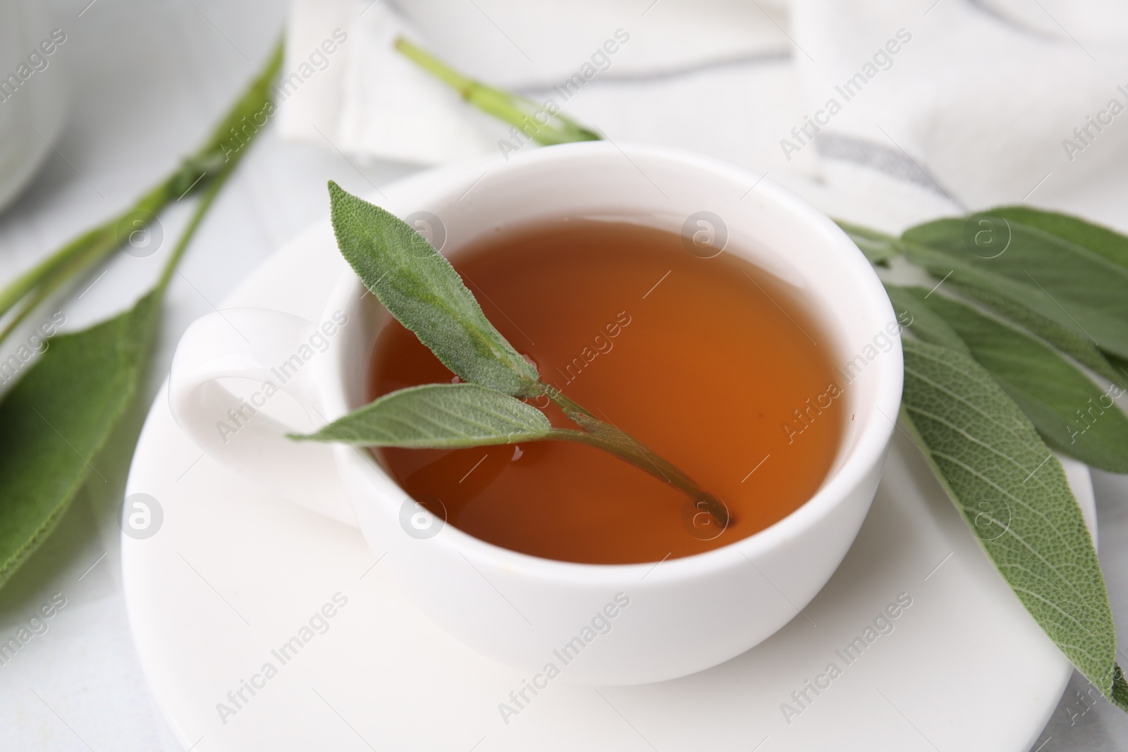 Photo of Aromatic herbal tea in cup with sage on white table