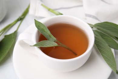 Aromatic herbal tea in cup with sage on white table