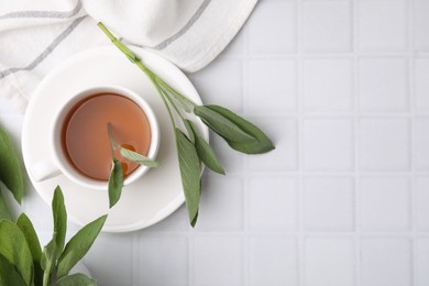 Aromatic herbal tea in cup with sage on white tiled table, flat lay. Space for text