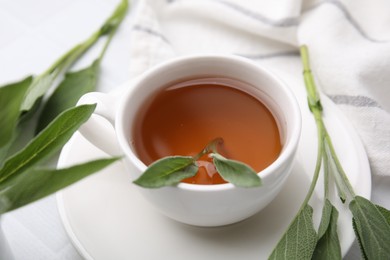 Photo of Aromatic herbal tea in cup with sage on white table, closeup