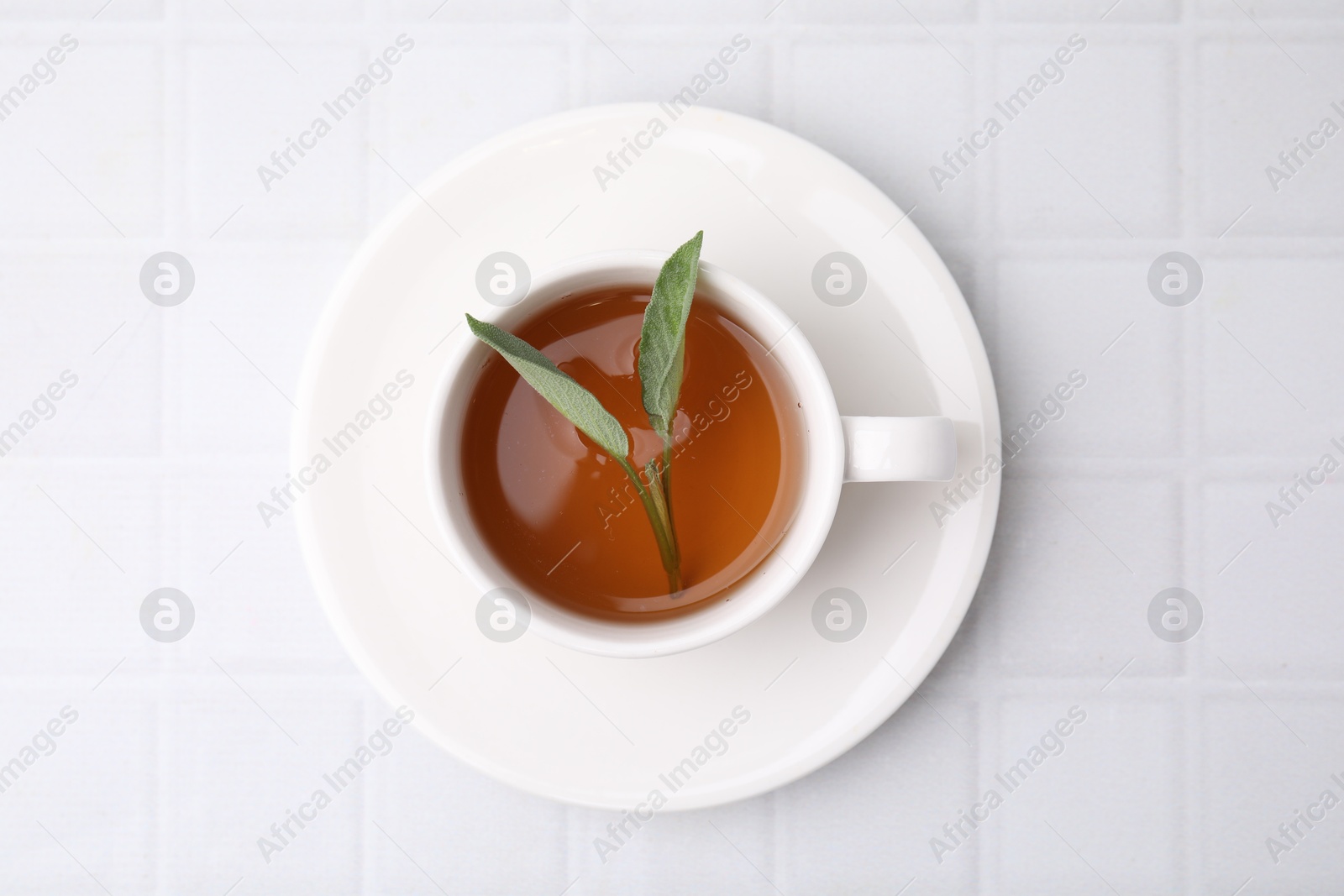 Photo of Aromatic herbal tea with sage in cup on white tiled table, top view