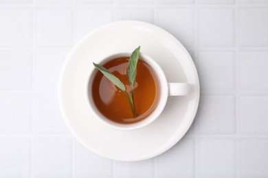 Aromatic herbal tea with sage in cup on white tiled table, top view