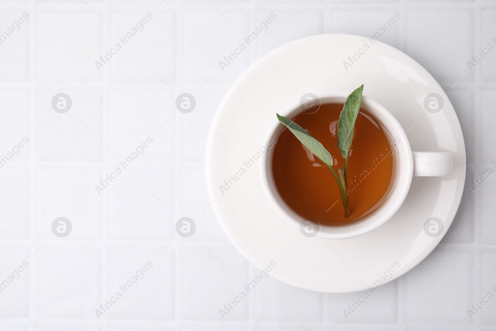 Photo of Aromatic herbal tea with sage in cup on white tiled table, top view. Space for text