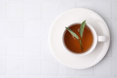 Aromatic herbal tea with sage in cup on white tiled table, top view. Space for text