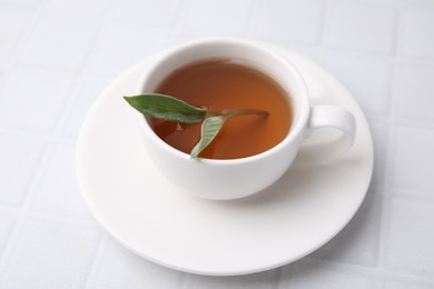 Aromatic herbal tea with sage in cup on white tiled table