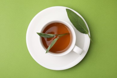 Photo of Aromatic herbal tea in cup with sage on green table, top view