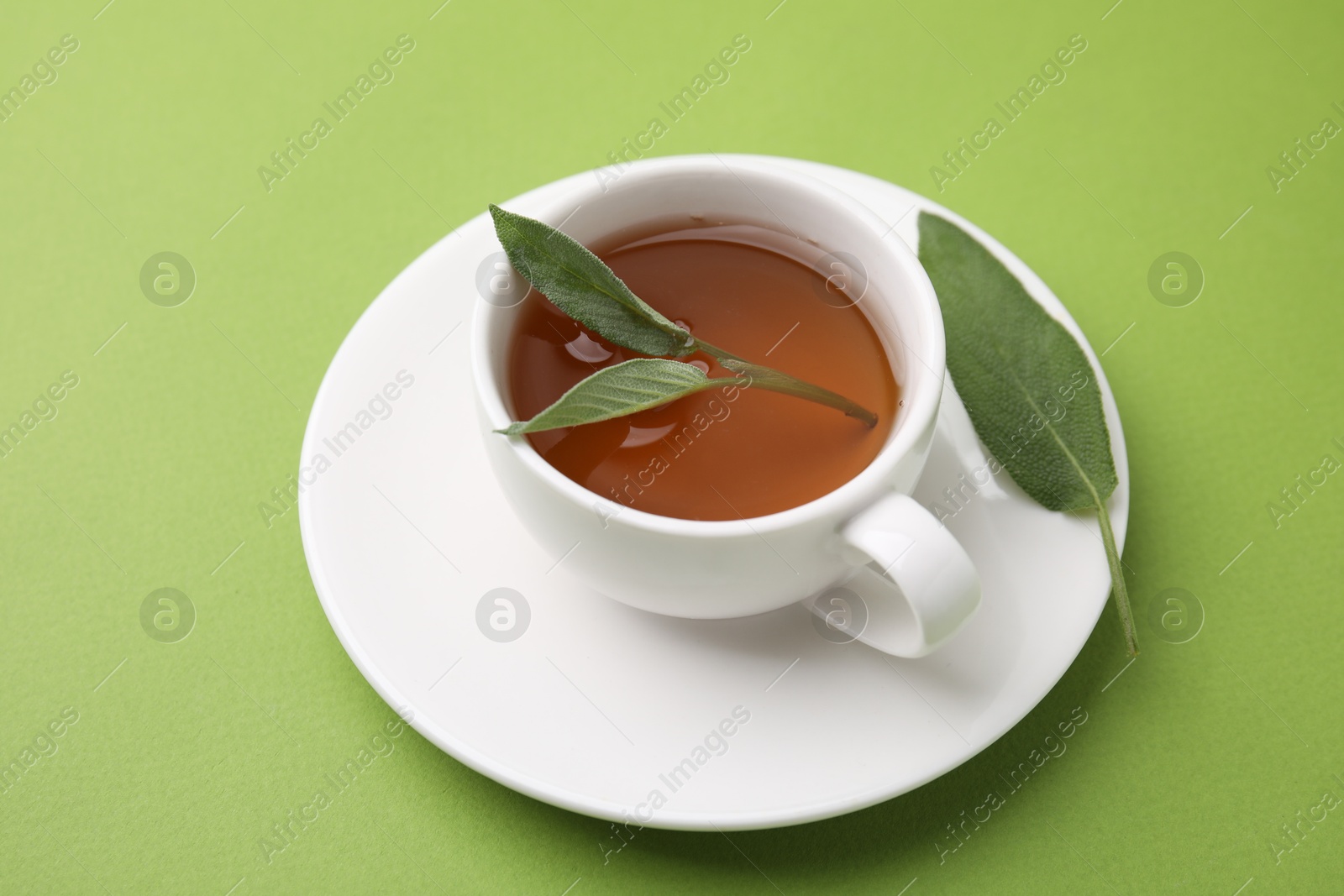 Photo of Aromatic herbal tea in cup with sage on green table