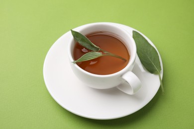 Photo of Aromatic herbal tea in cup with sage on green table