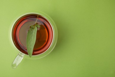 Aromatic herbal tea with sage in cup on green table, top view. Space for text