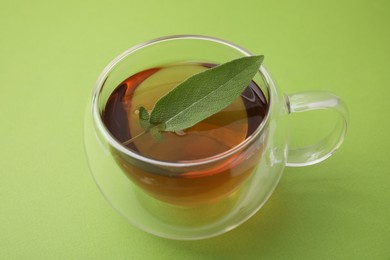 Aromatic herbal tea with sage in cup on green table