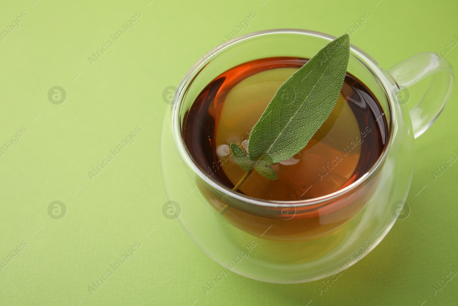 Photo of Aromatic herbal tea with sage in cup on green table. Space for text