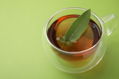 Aromatic herbal tea with sage in cup on green table. Space for text