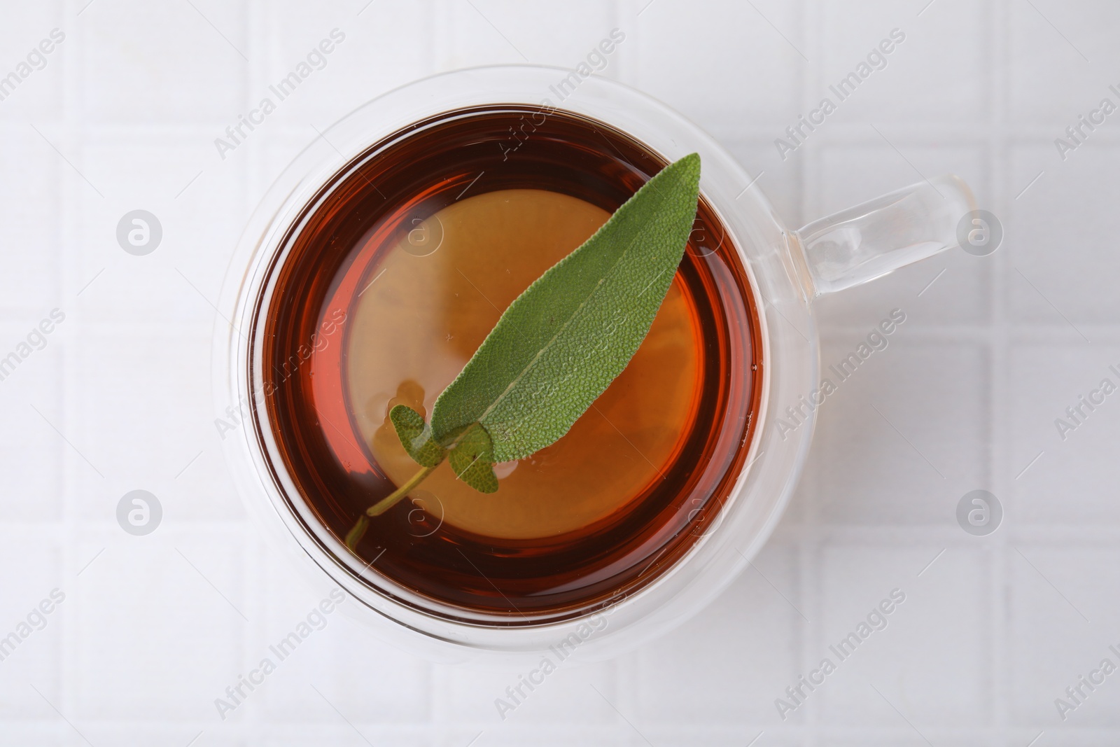 Photo of Aromatic herbal tea with sage in cup on white tiled table, top view