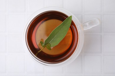 Aromatic herbal tea with sage in cup on white tiled table, top view