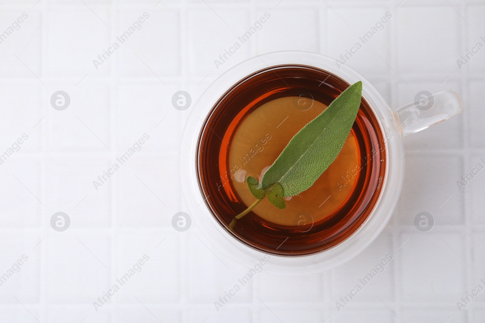 Photo of Aromatic herbal tea with sage in cup on white tiled table, top view. Space for text